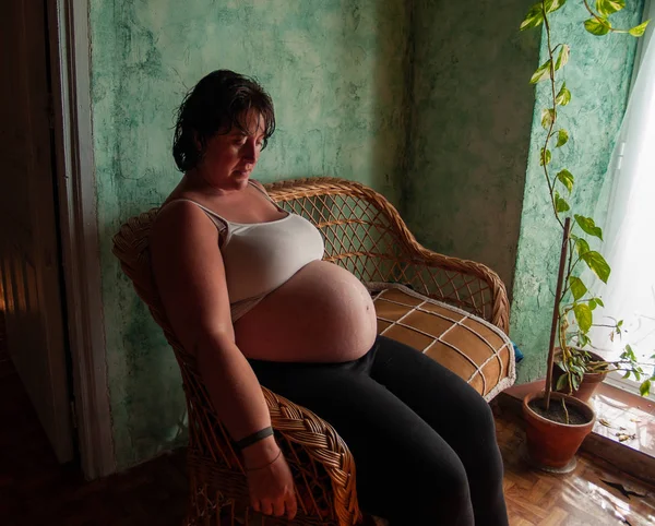 Female artist painting the belly of a pregnant young woman with body paints and brushes