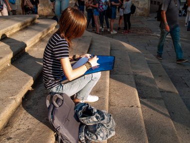 Genç bir kadın Üniversitesi Kampüsü merdivenlerde oturan bir klasördeki folio kalemle yazma