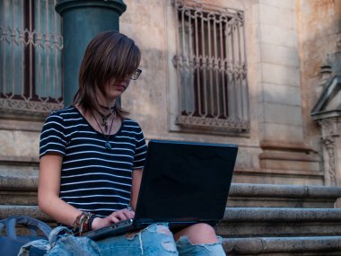 Bir üniversitede bir üniversite kampüsü merdiven üstünde a laptop ile okuyan bir genç kadın