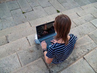 Bir üniversitede bir üniversite kampüsü merdiven üstünde a laptop ile okuyan bir genç kadın