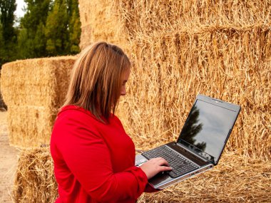 Bir saman balya çalışan bir dizüstü bilgisayar ile bir çiftlikte açık bir girişimci genç kadın