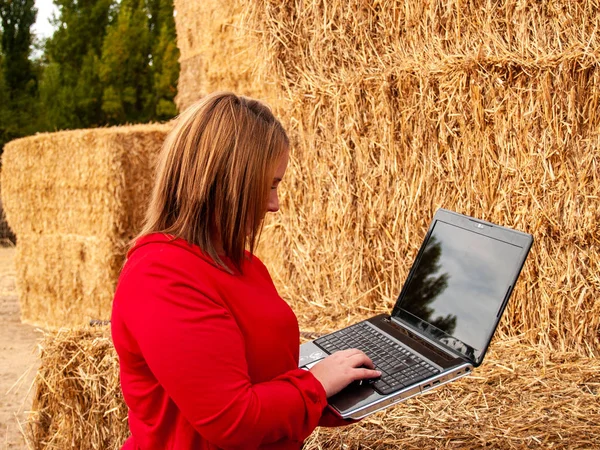 An entrepreneur young woman working outdoor on a farm with a laptop over a hay bale