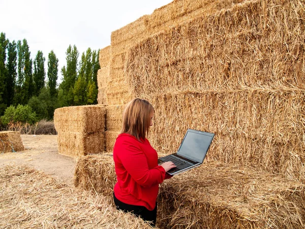 An entrepreneur young woman working outdoor on a farm with a laptop over a hay bale