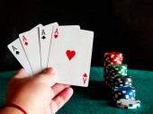 Člověk hrát poker s čtyři esa balíček v jeho rukou a poker žetonů různých barev na zelený mat