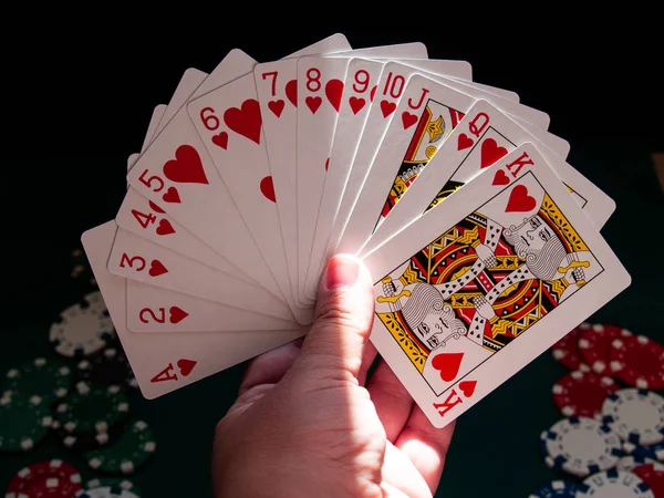 A person playing poker with a deck of poker cards in his hand and poker chips of various colors on a green mat