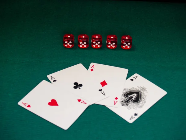 The four aces of a poker deck and several dice on a green mat