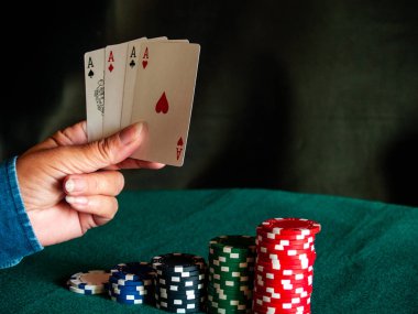 Bir kişi bir güverte dört as poker çeşitli renkler onun eli ve poker fiş yeşil bir mindere oynuyor.