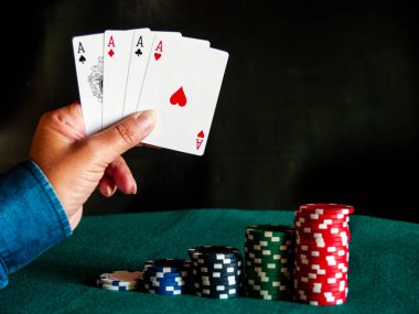 Bir kişi bir güverte dört as poker çeşitli renkler onun eli ve poker fiş yeşil bir mindere oynuyor.