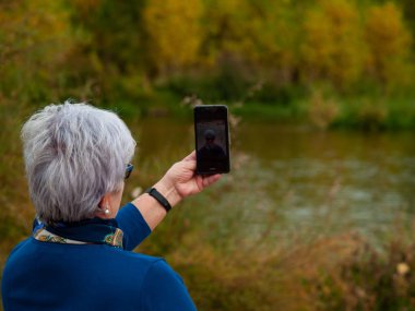 Gri saçlı selfies fotoğrafları üzerinde riverside sonbaharda alarak üst düzey bir kadın