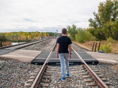 Tren rayları üzerinde yürüyen bir genç çocuk