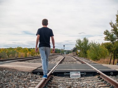Tren rayları üzerinde yürüyen bir genç çocuk