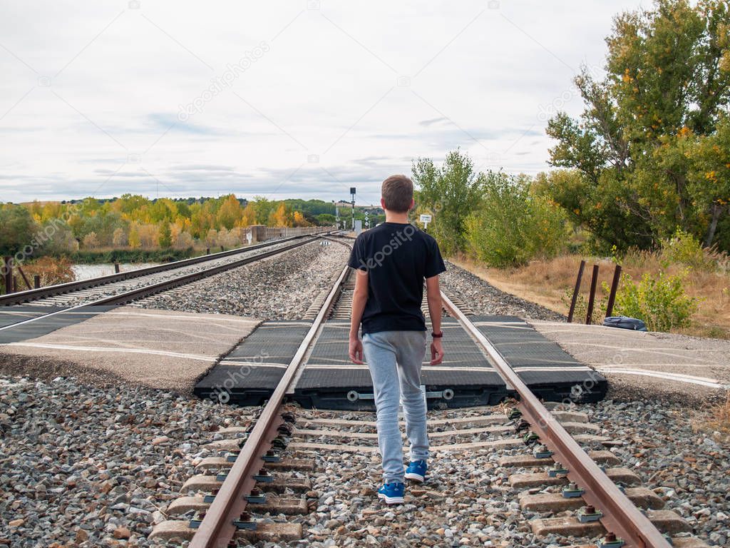 A teenage boy walking on the train tracks