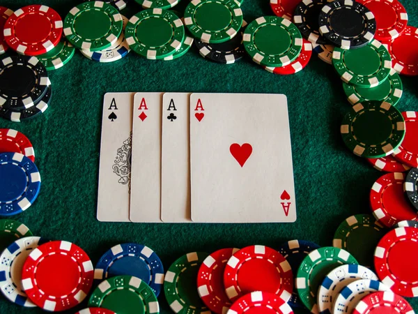 The four aces of a poker deck and poker chips of various colors on a green mat