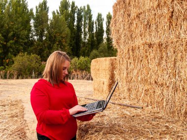 An entrepreneur young woman working outdoor on a farm with a laptop over a hay bale