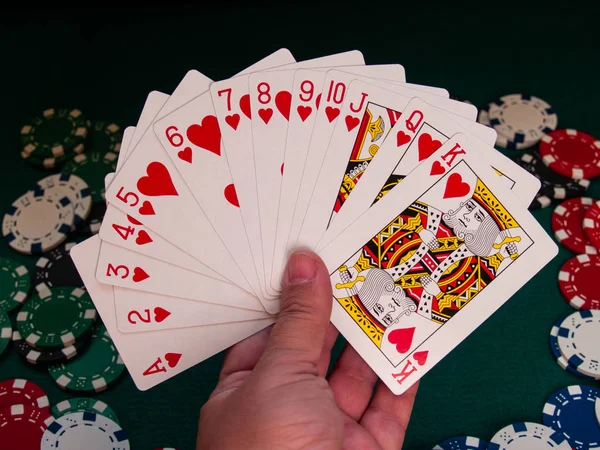 A person playing poker with a deck of poker cards in his hand and poker chips of various colors on a green mat