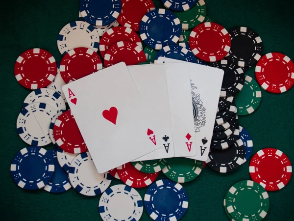 The four aces of a poker deck and poker chips of various colors on a green mat