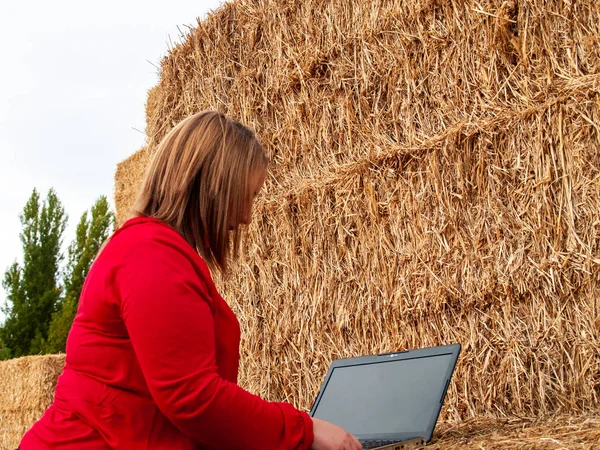 An entrepreneur young woman working outdoor on a farm with a laptop over a hay bale