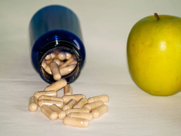 An apple and a blue container with vegetable fiber pills on a table