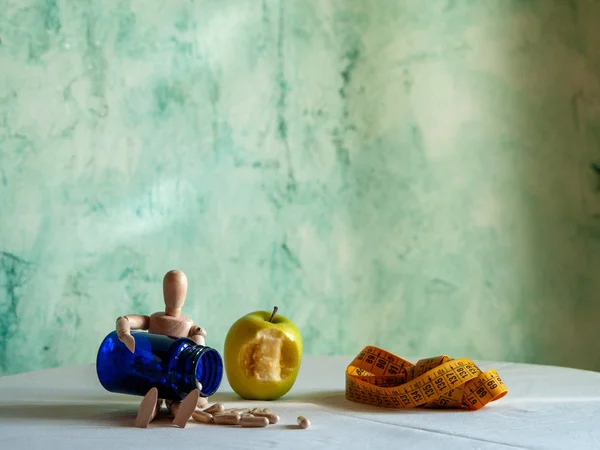 A figurine with a bitten apple, a tape measure and a blue container with vegetable fiber pills on a table