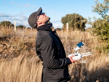 Bir dron pilot pilot ile smartphone ormanın içinde onun elinde uzaktan kumanda ile ve gökyüzüne bakarak
