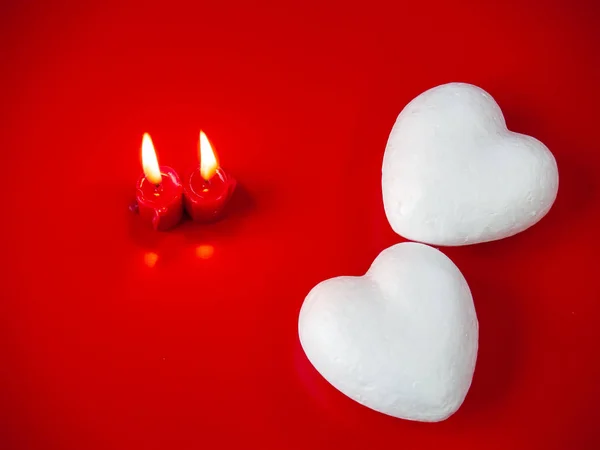 Concept of love Red candles lit and two poliespan hearts with a red background