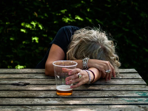 一个喝醉的女人 手里拿着一杯啤酒 不省人事 倚在桌子上 — 图库照片
