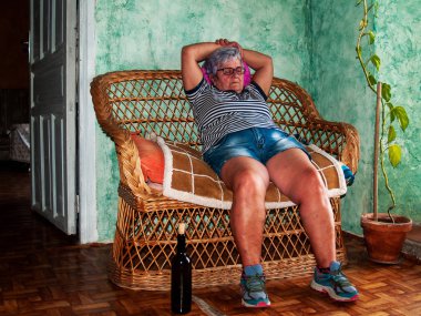 Sarhoş bir kadın kıdemli bir kanepe oturma onun elinde bir şişe şarap ile