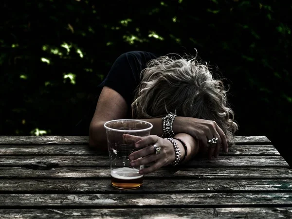 一个喝醉的女人 手里拿着一杯啤酒 不省人事 倚在桌子上 — 图库照片