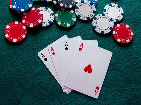 The four aces of a poker deck and poker chips of various colors on a green mat