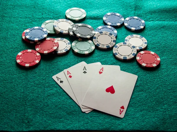 The four aces of a poker deck and poker chips of various colors on a green mat