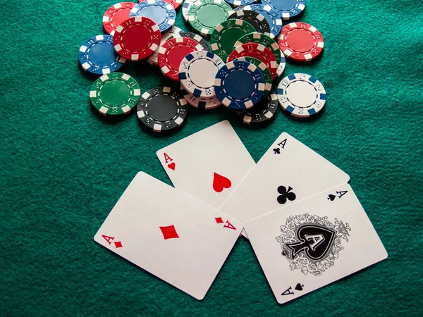 The four aces of a poker deck and poker chips of various colors on a green mat