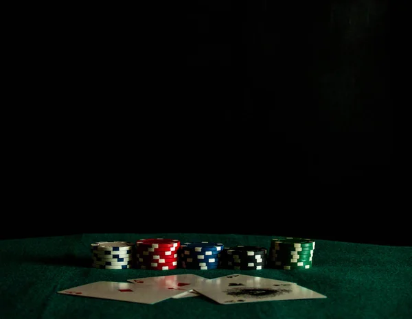 The four aces of a poker deck and poker chips of various colors on a green mat