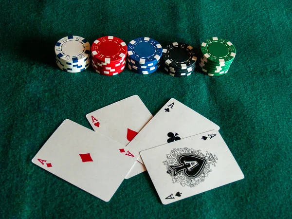 The four aces of a poker deck and poker chips of various colors on a green mat