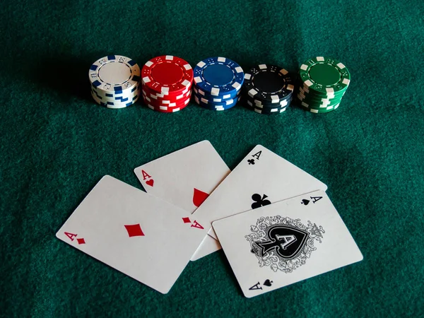 The four aces of a poker deck and poker chips of various colors on a green mat