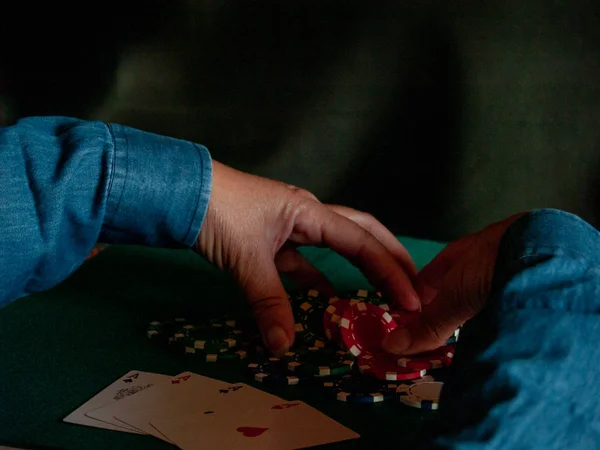 A person playing poker with the four aces of a deck in his hand and poker chips of various colors on a green mat