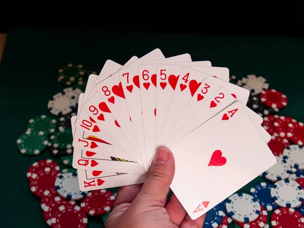 A person playing poker with a deck of poker cards in his hand and poker chips of various colors on a green mat