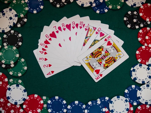 A deck of poker cards and poker chips of various colors on a green mat