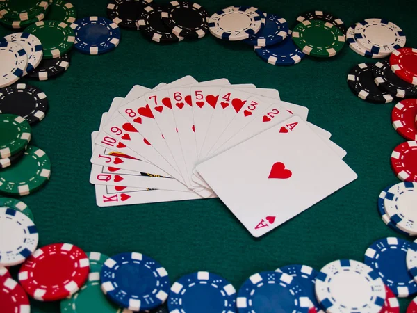 A deck of poker cards and poker chips of various colors on a green mat