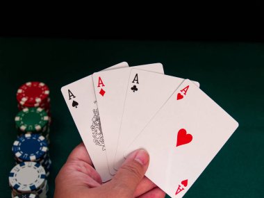 Bir kişi bir güverte dört as poker çeşitli renkler onun eli ve poker fiş yeşil bir mindere oynuyor.