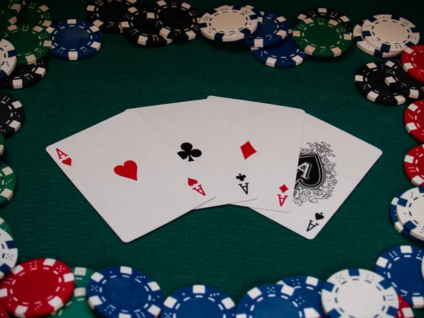 The four aces of a poker deck and poker chips of various colors on a green mat