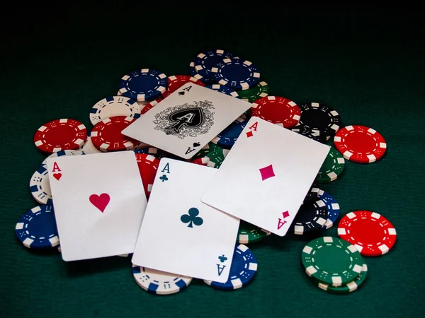 The four aces of a poker deck and poker chips of various colors on a green mat