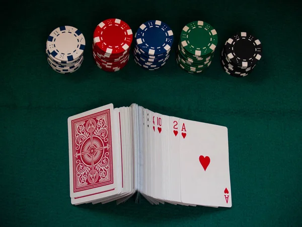 A deck of poker cards and poker chips of various colors on a green mat
