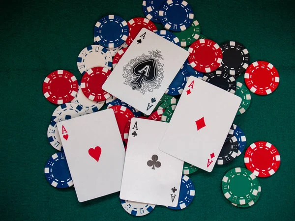 The four aces of a poker deck and poker chips of various colors on a green mat