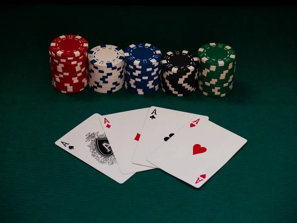 The four aces of a poker deck and poker chips of various colors on a green mat