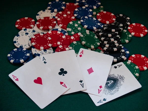 The four aces of a poker deck and poker chips of various colors on a green mat