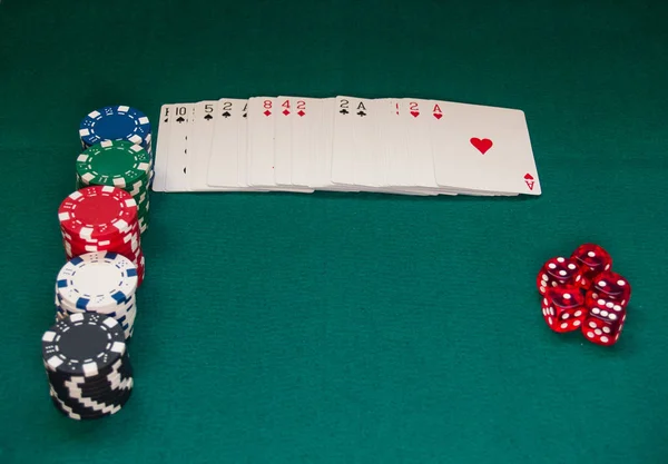 A poker deck, poker chips of different colors and several dice on a green mat