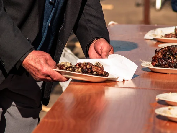 Unrecognizable person taking meat cooked from a paper plate in the street at a popular party in a village in Spain