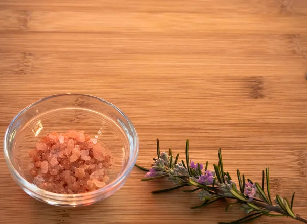 Crystal bowls with himalayan pink salt and rosemary blooming twig on a wooden table