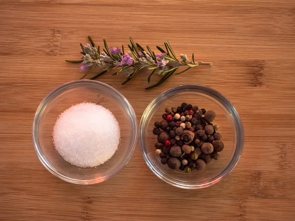 Crystal bowls with common marine salt, five peppercorns mix and rosemary on a wooden table