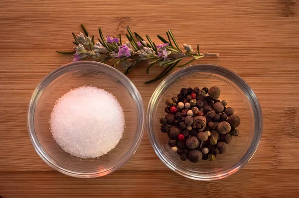 Crystal bowls with common marine salt, five peppercorns mix and rosemary on a wooden table